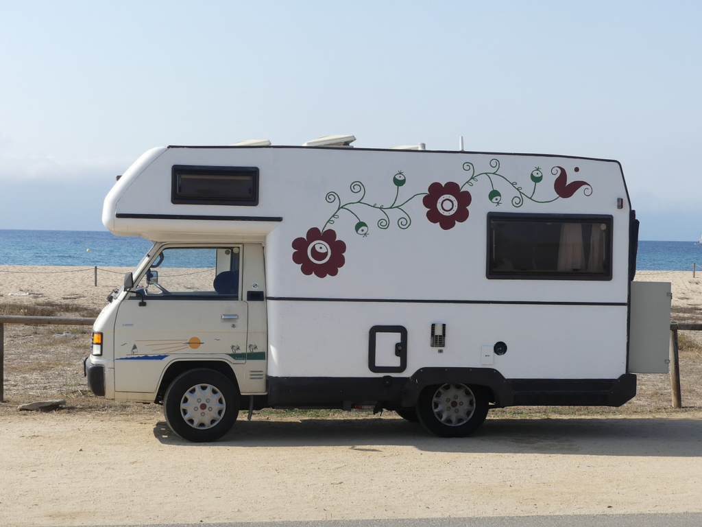 An RV parked by the beach, artwork of flowers and vines painted on the side.