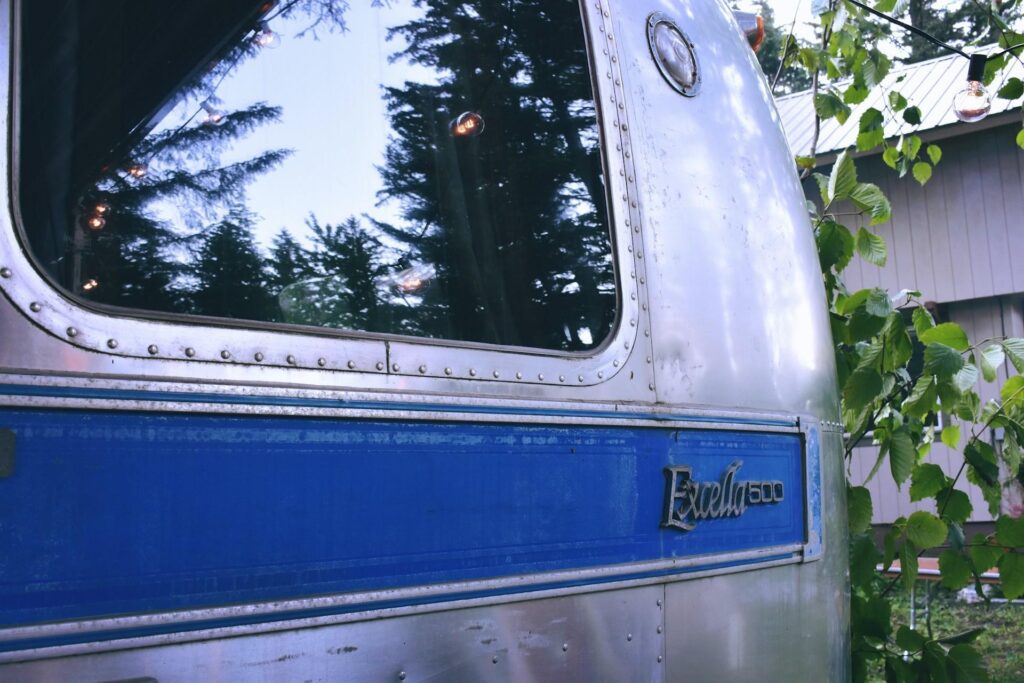 A reflective window on an Airstream trailer, showing the surrounding trees, with the logo "Excella 500" visible.