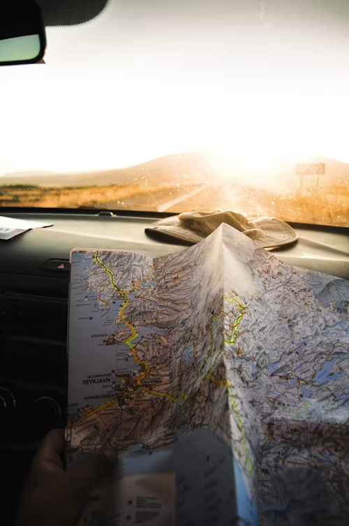 A person looking at a map inside a car, with a sunny horizon in the background.