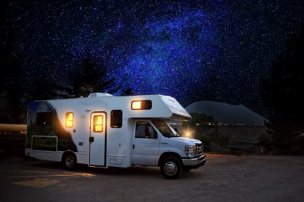 A motorhome parked on an empty site at night, with the lights inside on and a starlit sky above.