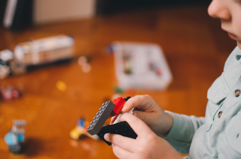 A child playing with LEGO pieces, focusing on a small build, with a blurred background of more LEGO pieces.