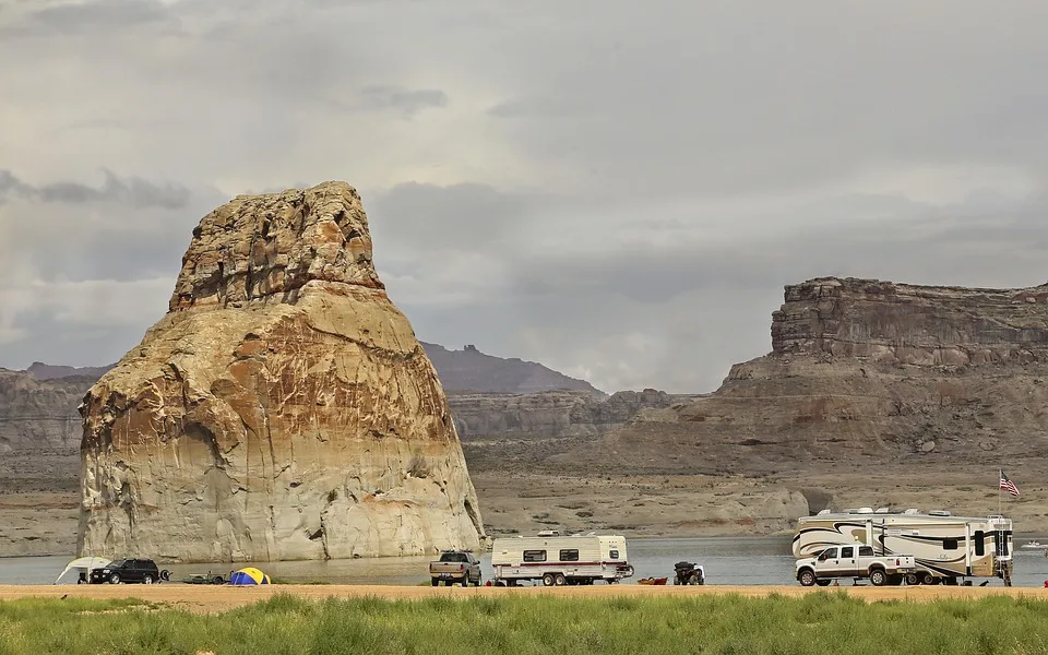 An RV parked under a starry night sky with its interior lights on, set against a backdrop of trees and mountains.