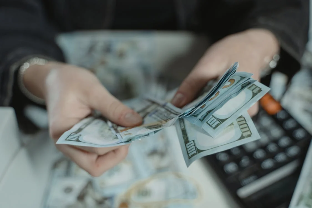 A close-up shot of a person’s hands counting a stack of $100 bills.