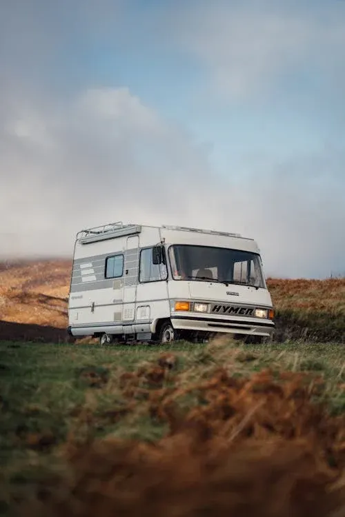 A white motorhome parked on a grassy hill under a cloudy sky.