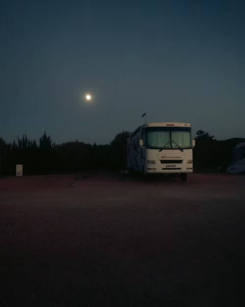 A motorhome parked in a dark area at night, with the moon visible in the sky.