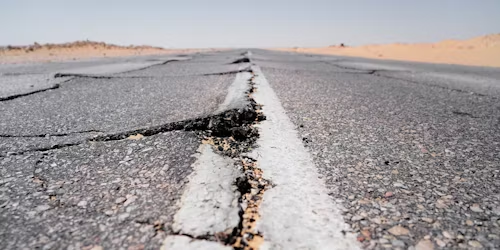 A close-up view of a cracked asphalt road with sand visible in the background.