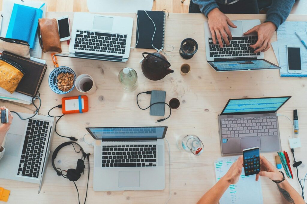 An overhead view of a workspace with multiple laptops, notebooks, and various items on a wooden table.