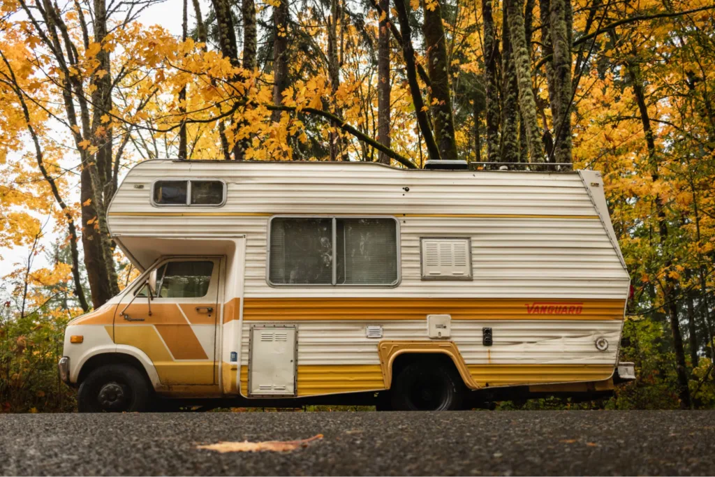 A vintage RV branded "Vanguard" parked on a road with autumn foliage and trees in the background.