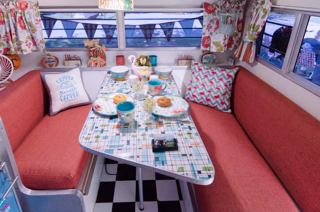 A retro-themed camper van interior with a vibrant dining setup, including plates, cups, and breakfast food on the table.