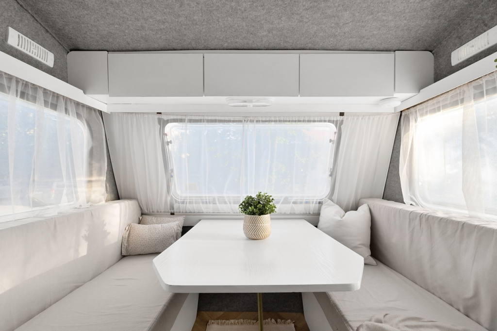 The interior of a campervan with a clean, white dining area featuring a table, bench seating, and a small potted plant.