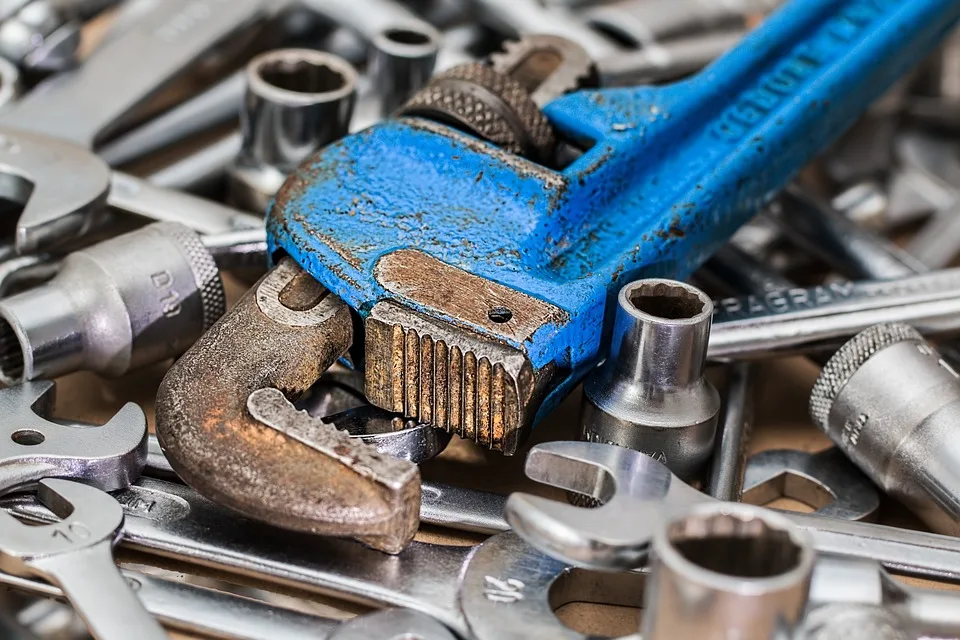 A weathered blue pipe wrench lying on top of a pile of various wrenches and sockets.