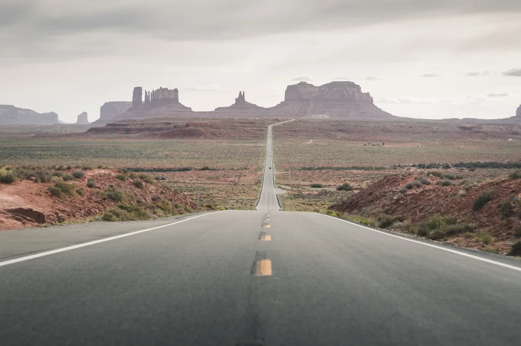 A straight, open road leading towards distant rock formations in a desert landscape.