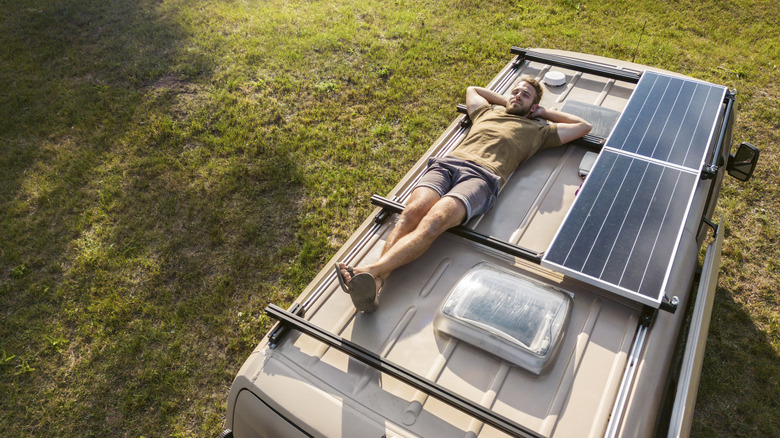 Man lying on his back on top of a camper van. Late summer time with sunshine