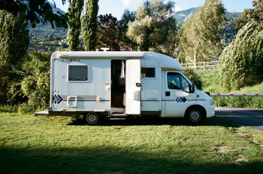 A motorhome parked in a green area with trees and mountains on the background