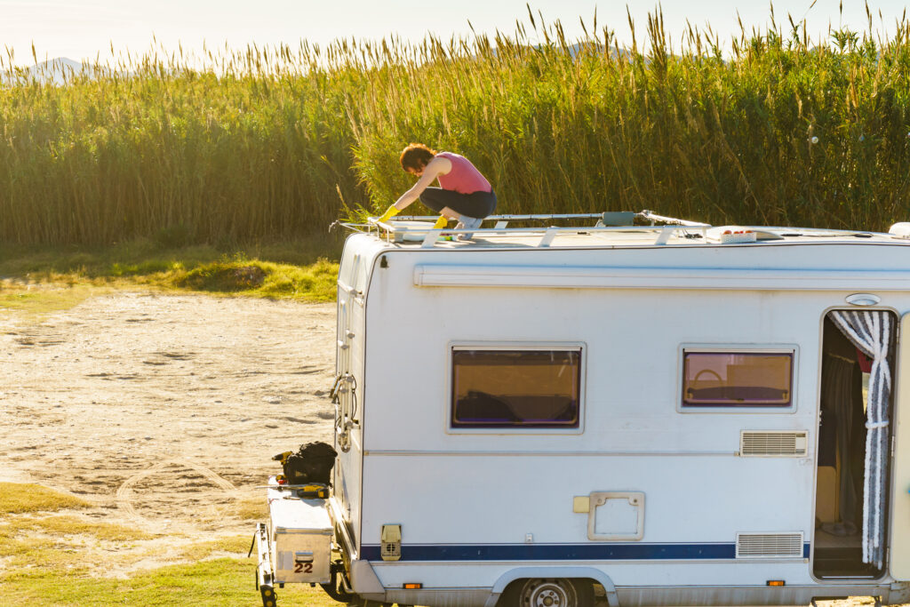 A person working on the roof of a motorhome parked in a field, surrounded by tall grass.