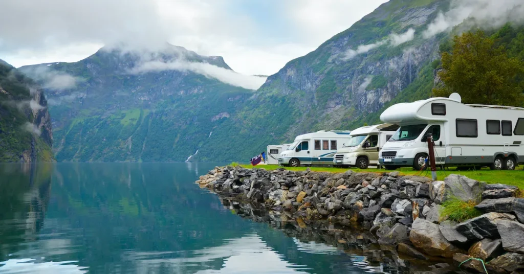 Different RVs parked by the picturesque lake with the mountains on a background.