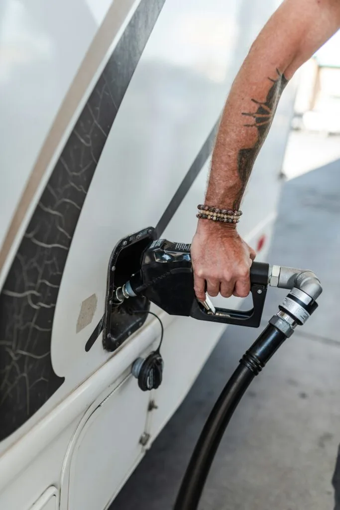 A close-up of a person with tattooed and beaded arm filling up an RV with fuel at a gas station.