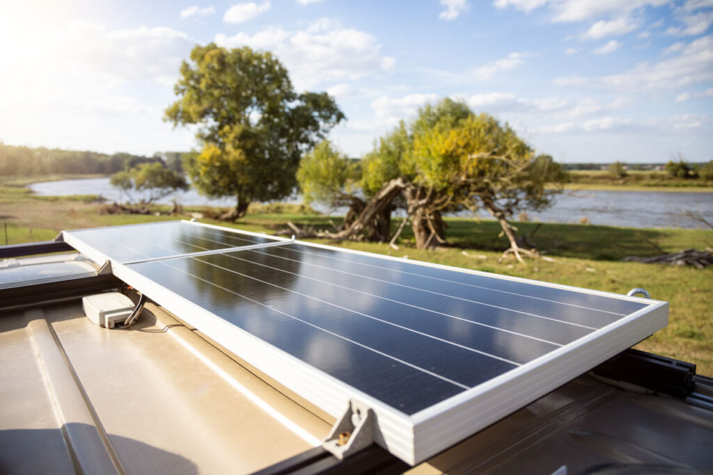 A solar panel on the roof of a camper van parked in nature. Sunny day with trees and a river in the background.