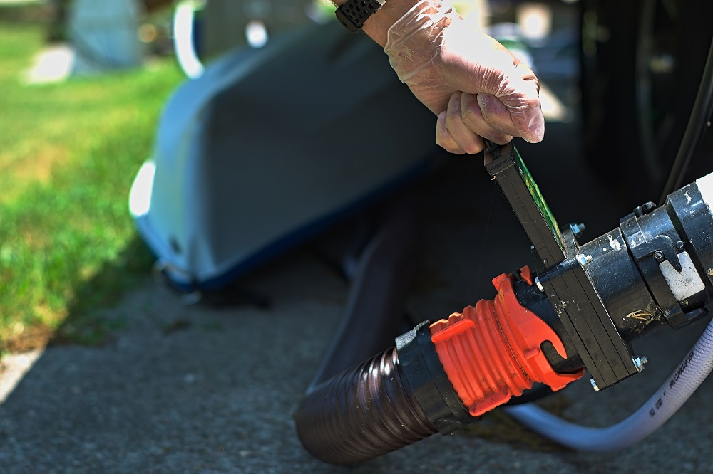 A person with gloves handling the sewage hose connection on an RV or travel trailer, preparing for waste disposal.