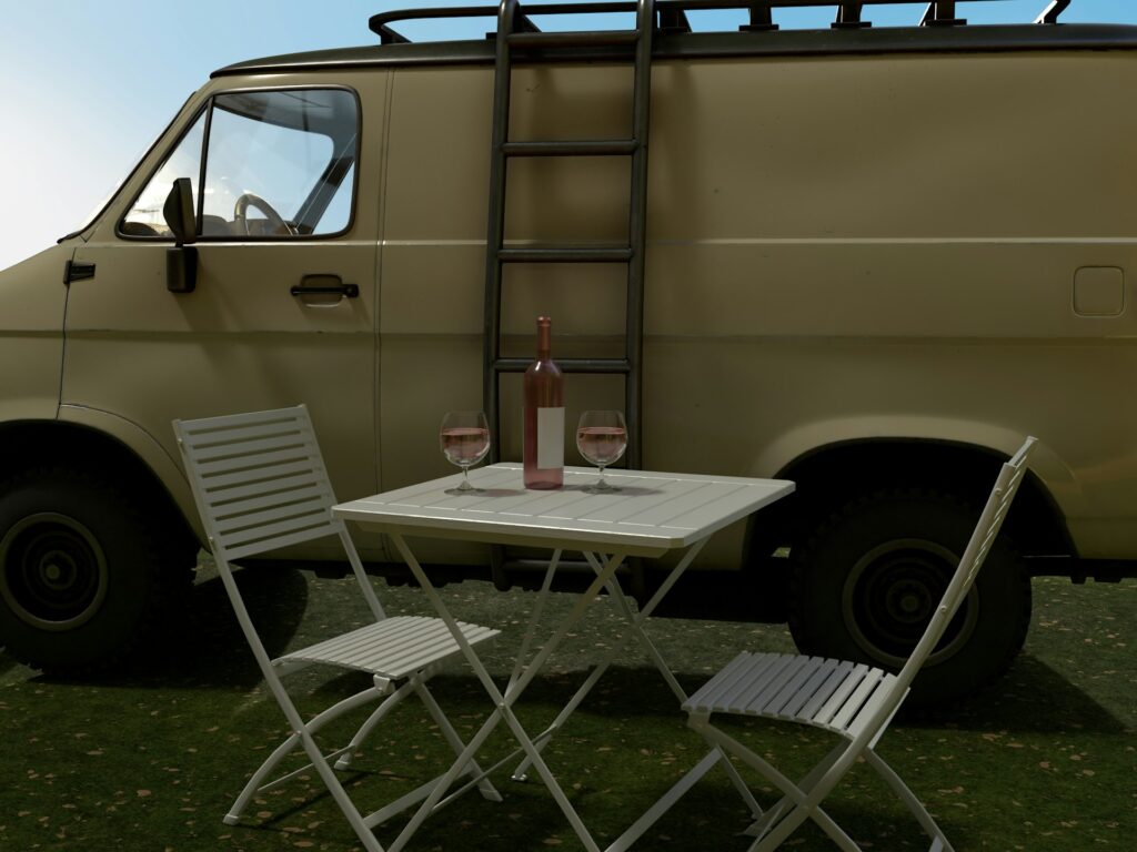 A folding table and chairs set up outside next to a van, with a bottle of wine and two filled wine glasses on the table.