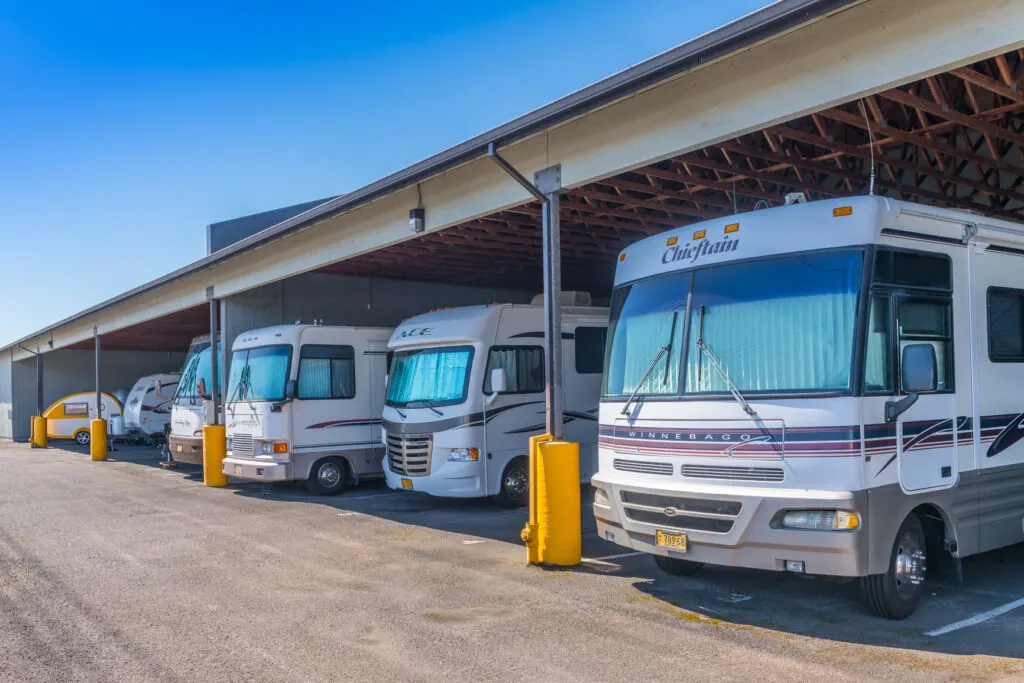 Several motorhomes and RVs parked under a large covered storage area in a parking lot.