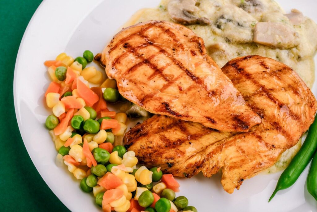 A plate with grilled chicken, mixed vegetables, and creamy sauce with mushrooms.