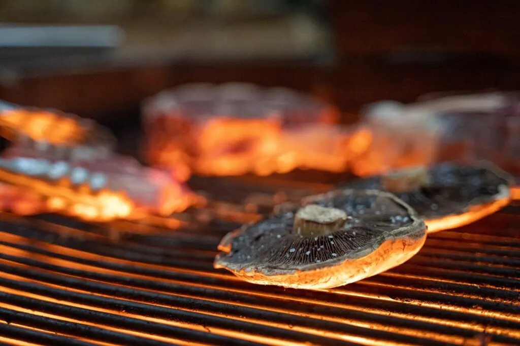 Portobello mushrooms grilling on an open flame. 