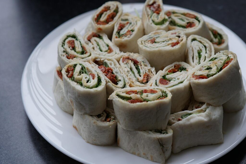 A plate of pinwheel sandwiches made with tortilla wraps, filled with lettuce and dried tomatoes.