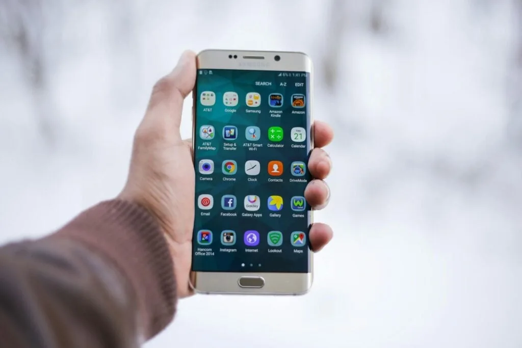 A person holding a smartphone displaying various app icons on the home screen.