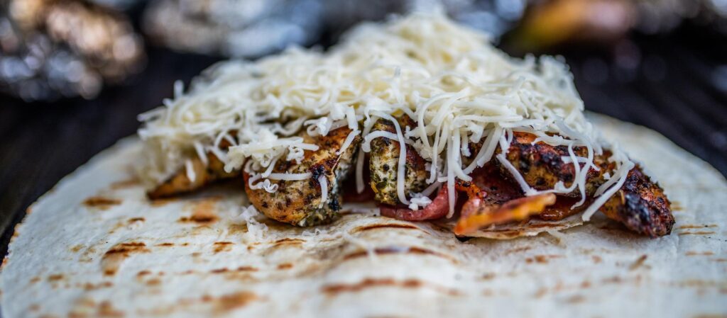 A grilled tortilla filled with marinated and grilled shrimp, topped with a generous amount of shredded cheese.