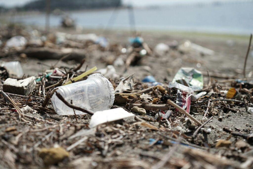 A beach littered with various pieces of trash, including plastic cups and wrappers, with the ocean in the background out of focus.