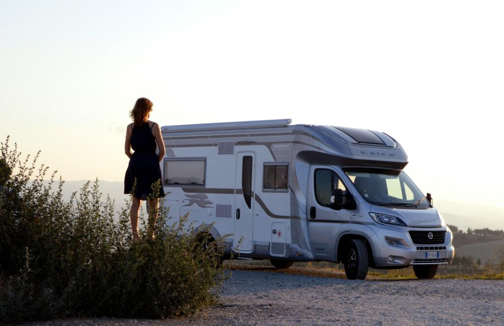 A person standing beside a parked camper van, looking at the horizon during sunset.