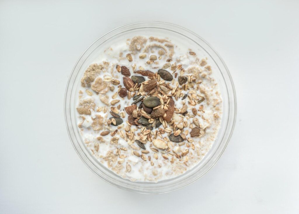 A bowl of cereal with milk, topped with granola, nuts, and seeds.