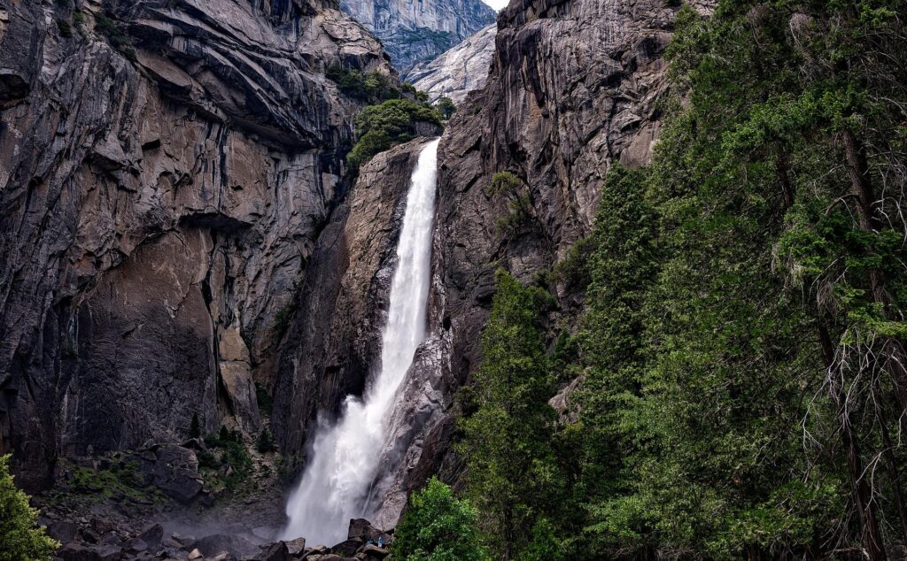 A powerful waterfall cascading down steep rock cliffs, surrounded by lush green trees and foliage in Yosemite National Park