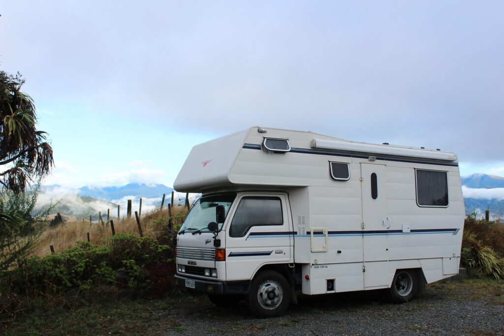 A white RV parked in a natural setting with mountains and blue sky in the background.