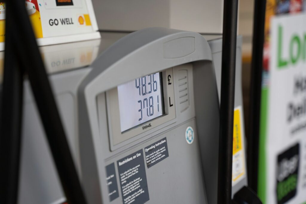 A close-up view of a fuel pump display showing an amount of £48.36 for 37.081 liters of fuel. The display is set against the backdrop of a fueling station.