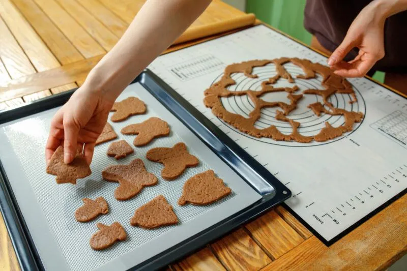 A person is putting raw cookies on a silicone baking mat.