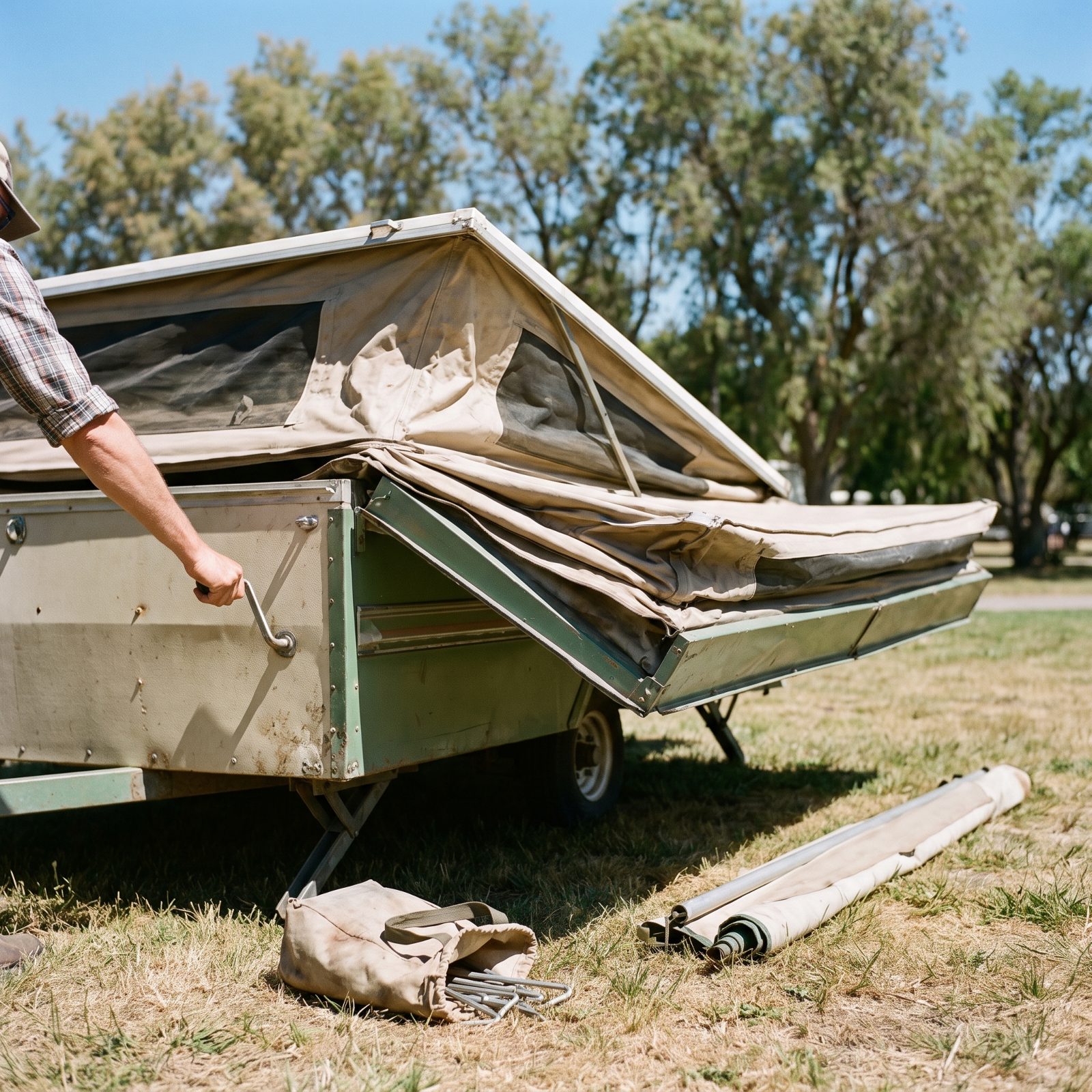 Campsite with a pop-up tent trailer, canvas sides extended and roof raised, a hand crank on the side.